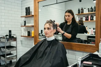 Femme aux cheveux enroulés sur des bigoudis de permanente dans un salon de coiffure moderne, styliste en action en arrière-plan